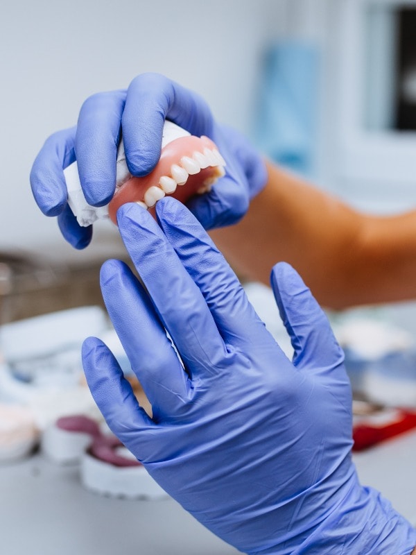 Dental prosthesis, prosthetics work. Close up of prosthetic's hands while working on the denture. Selective focus.