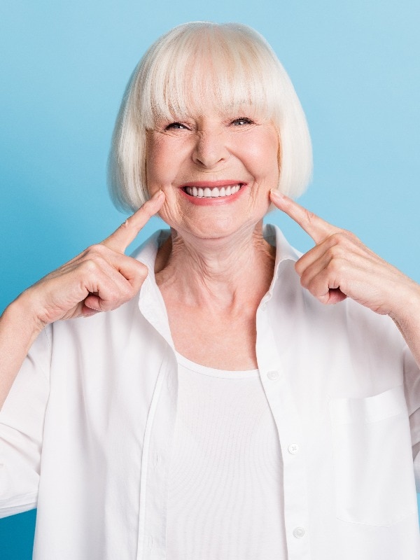 Photo portrait of granny blonde hair pointing at white teeth healthy smile dental whitening veneers isolated on bright blue color background